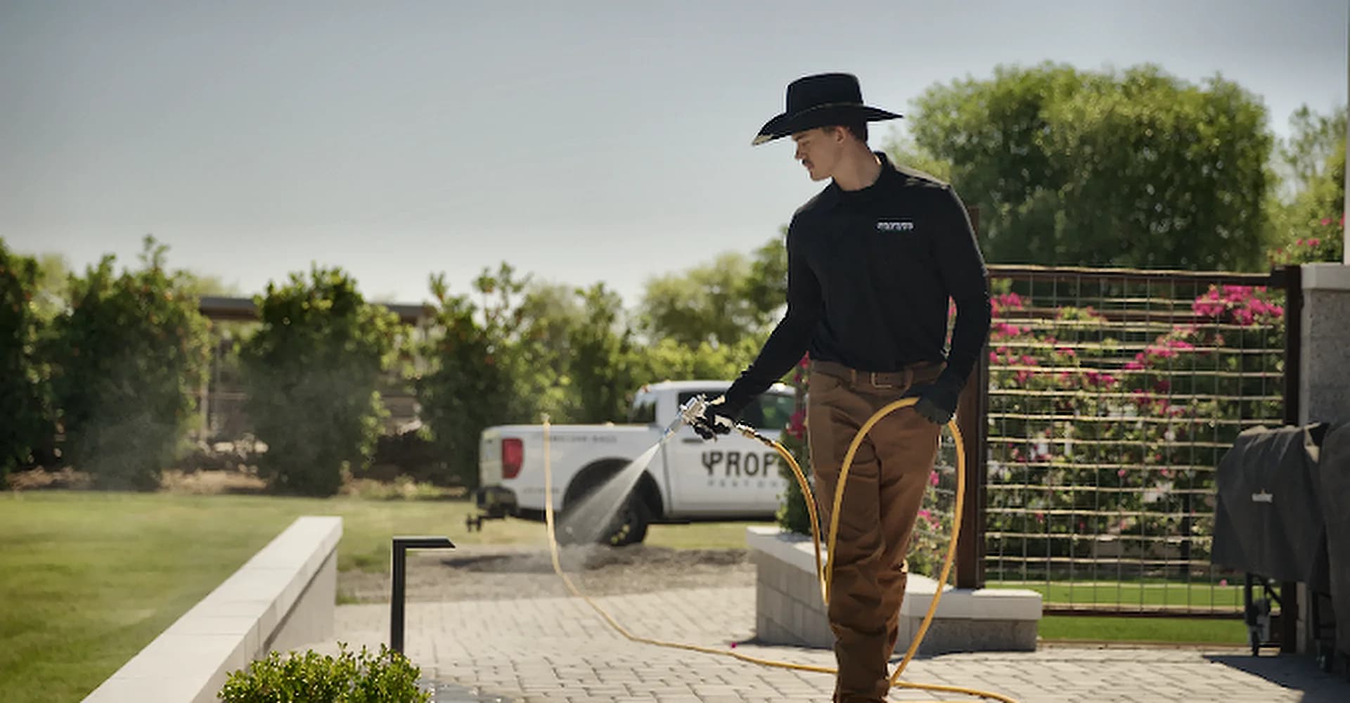 A Property Pest Control technician treating a Phoenix-area backyard, with the service truck parked behind